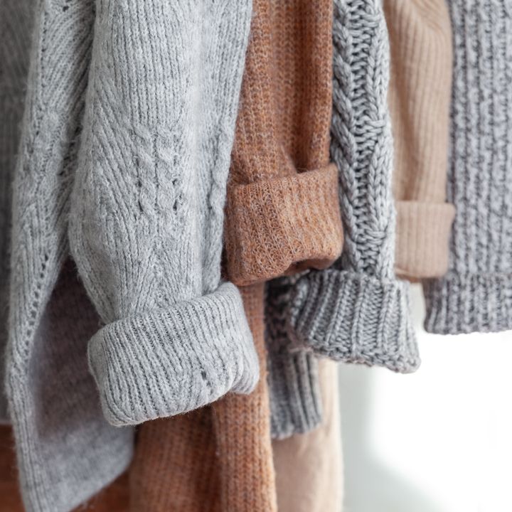 Several wool sweaters are hanging with their sleeves in a row, all in neutral colors.