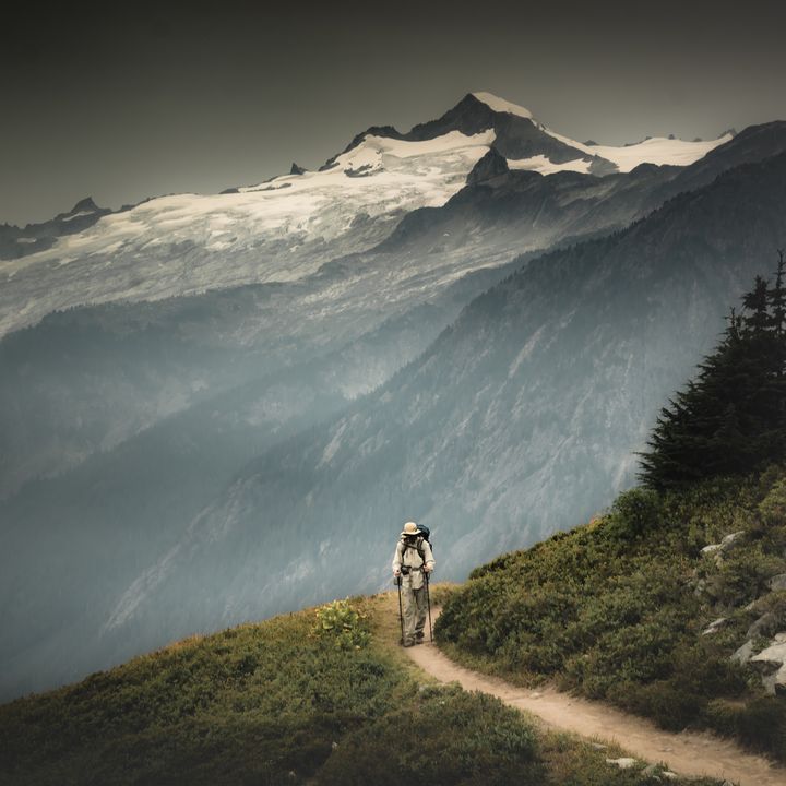 A male hiker is hiking through a valley pass on the back of snowy mountains in North Cascades National Park, Washington.
