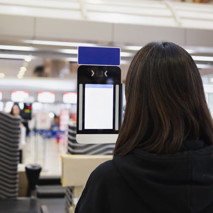 A woman is seen using a facial scanner at the airport with only the back of her head visible.