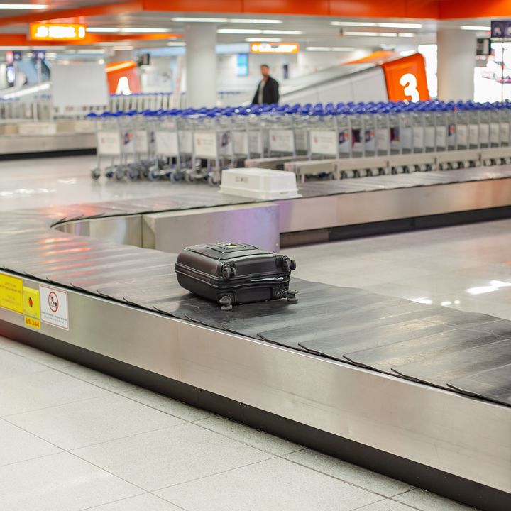 An empty luggage conveyor belt is seen with just one suitcase on it surrounded by airport luggage carts.