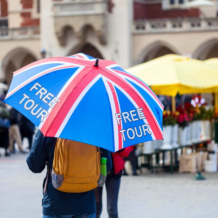 A tour guide holding a UK flag-themed umbrella that says free tour is seen in a European-looking square.