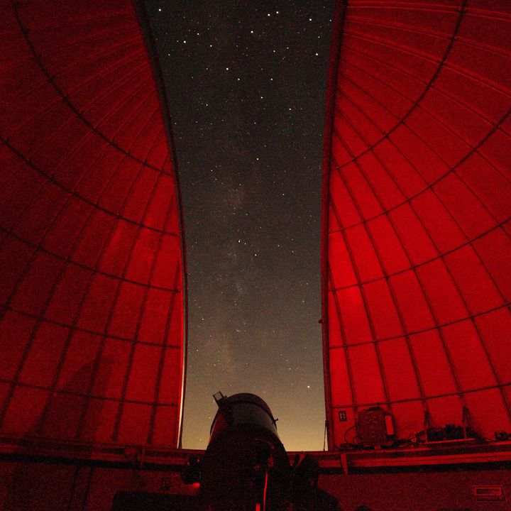 Looking out from inside an observatory with a sliver or stars and the interior lit up in red lights.