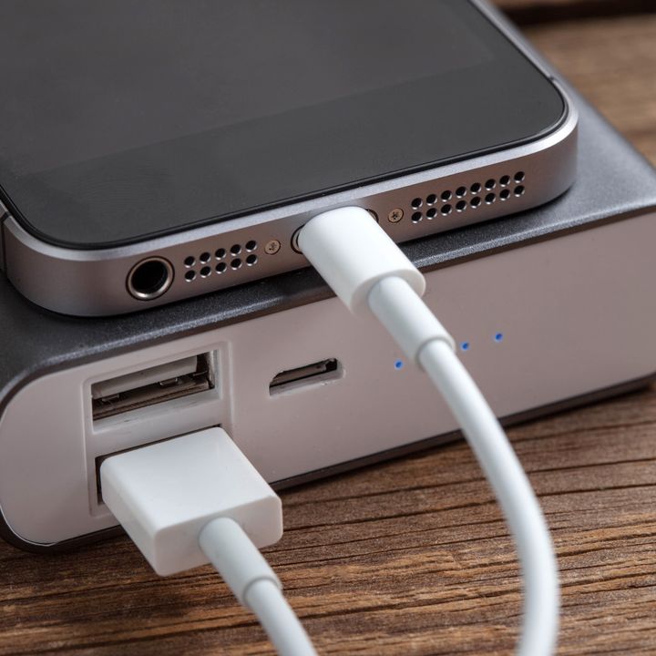 A power bank is charging an iPhone with it stacked on top of it, connected by a cord, sitting on a wood surface.