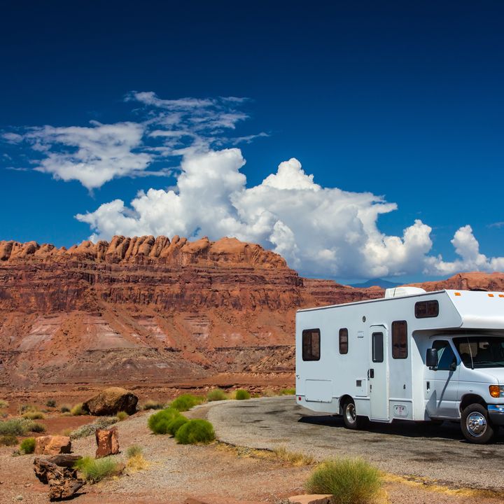 A white RV is seen parked in Canyonlands National Park, Utah, next to red rock formations.