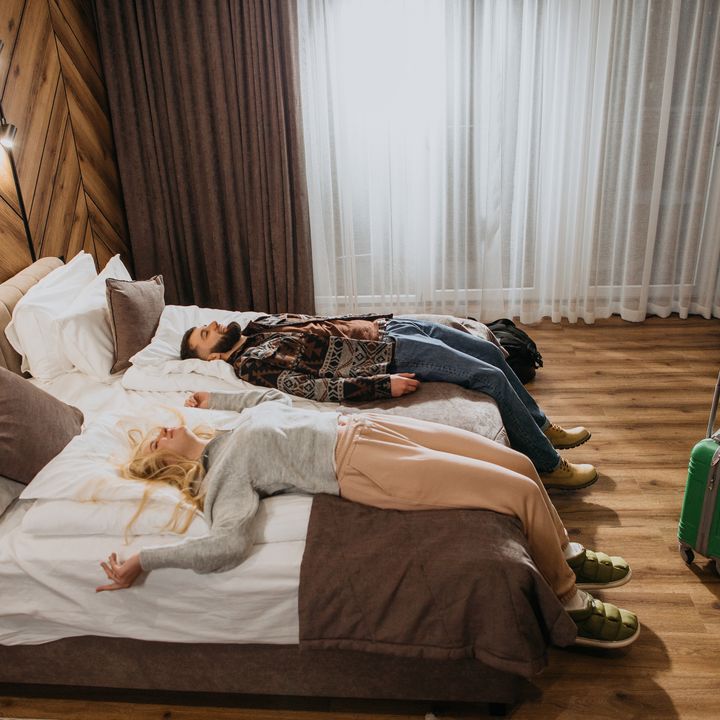 Couple relaxing on a bed with a suitcase near their feet.