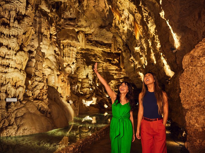 Two women walk inside a cavern and are seen admiring their surroundings.