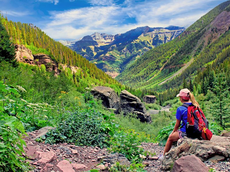 A hiker rests on a rock at the top of the Bear Creek Trail in Telluride, Colorado, during summer.