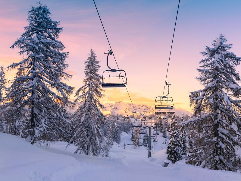 A chairlift is visible over a snowy mountain at sunset in winter.