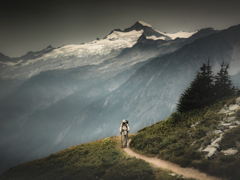 A male hiker is hiking through a valley pass on the back of snowy mountains in North Cascades National Park, Washington.